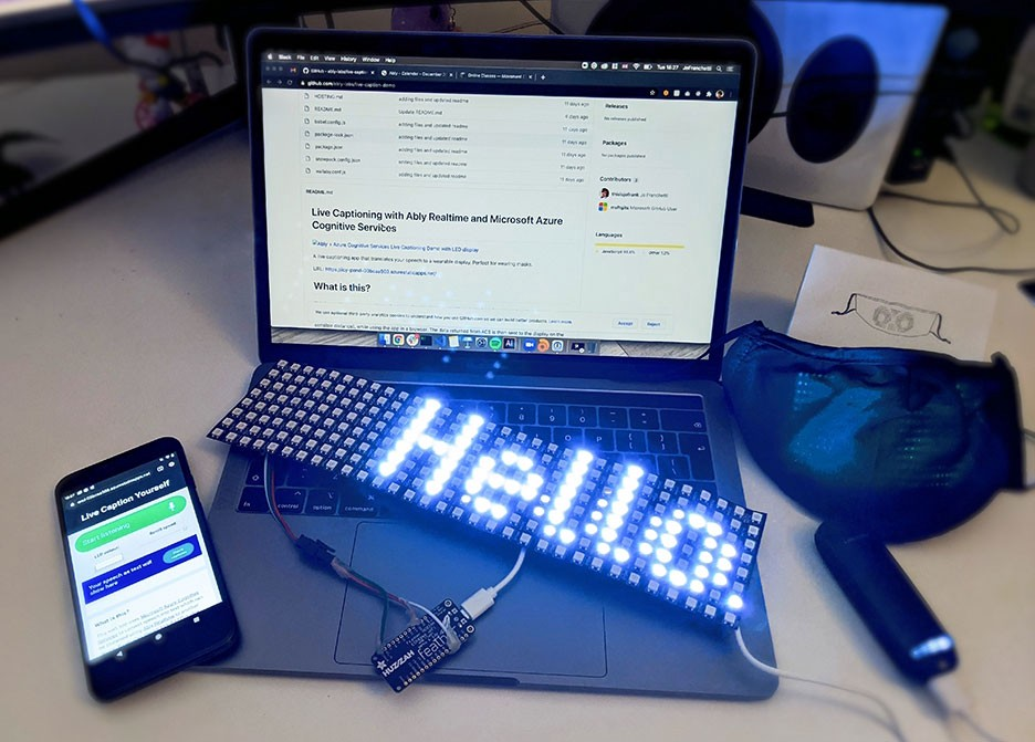 A flexible LED display connected to a microprocessor with a phone and a laptop and a small lipstick battery on a desk.